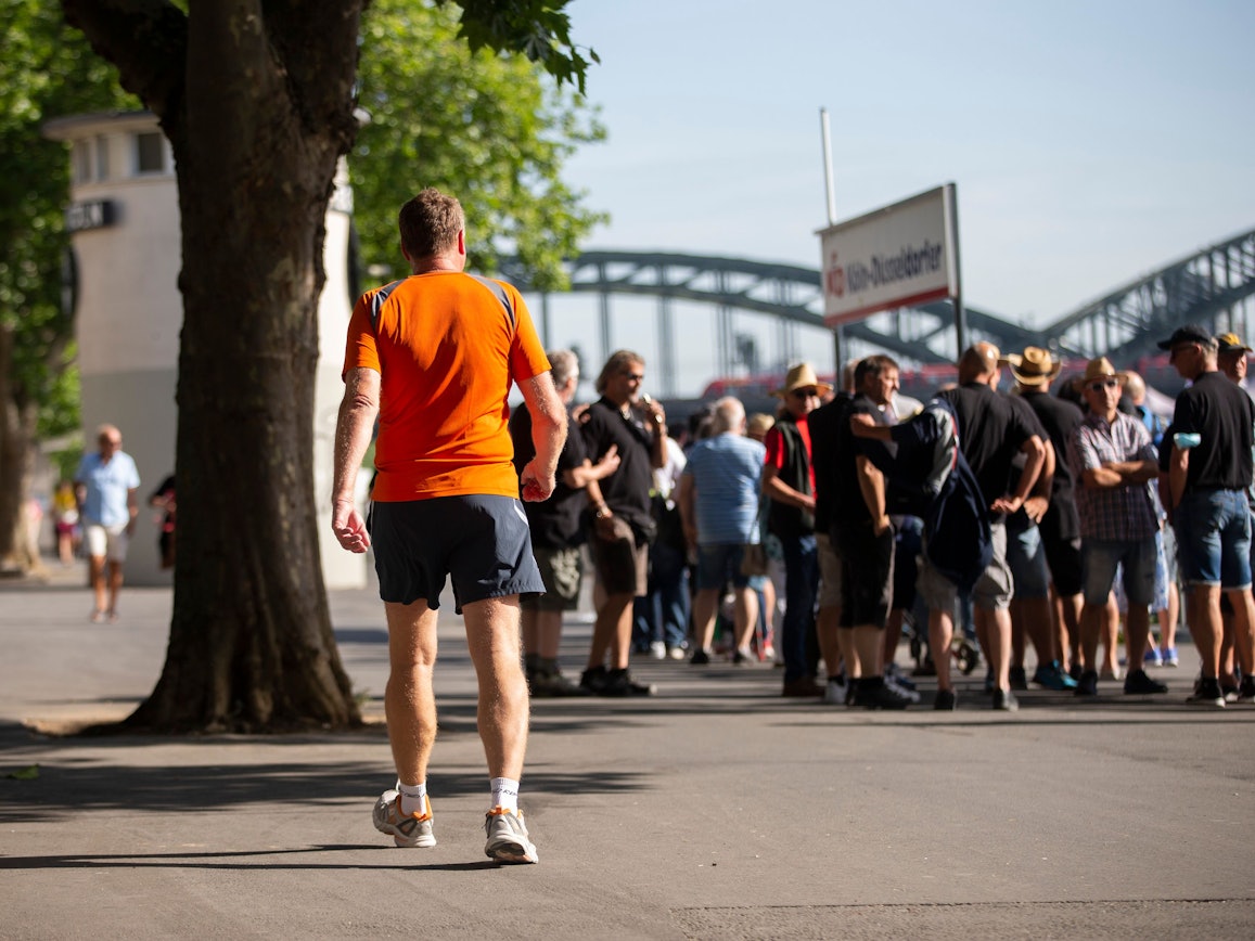 Touristinnen und Touristen stehen an der Kölner Rheinuferpromenade an, um mit einem Ausflugsschiff auf dem Rhein zu fahren.