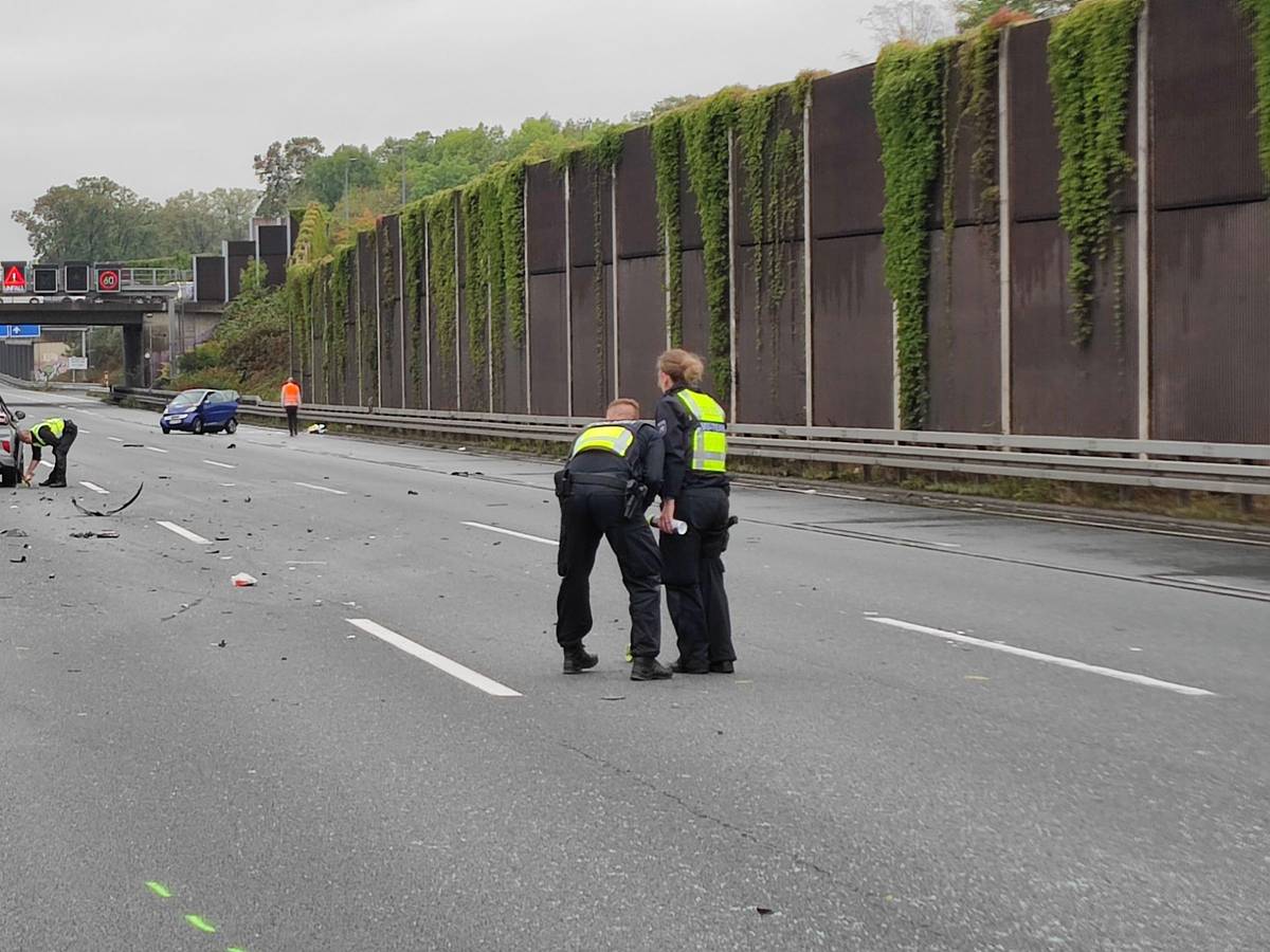 Die drei Unfallautos stehen umgeben von Trümmerteilen verteilt auf der Autobahn, Einsatzkräfte der Polizei stehen um die Autos herum.
