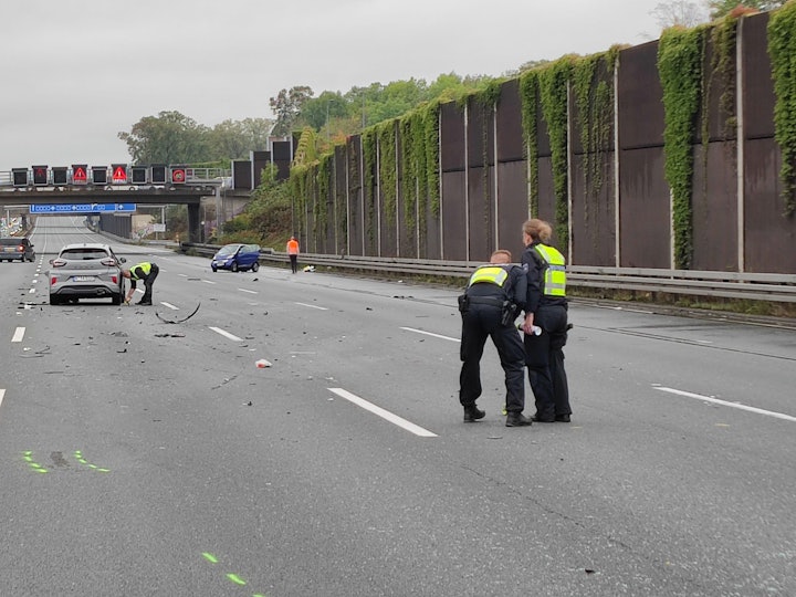 Die drei Unfallautos stehen umgeben von Trümmerteilen verteilt auf der Autobahn, Einsatzkräfte der Polizei stehen um die Autos herum.