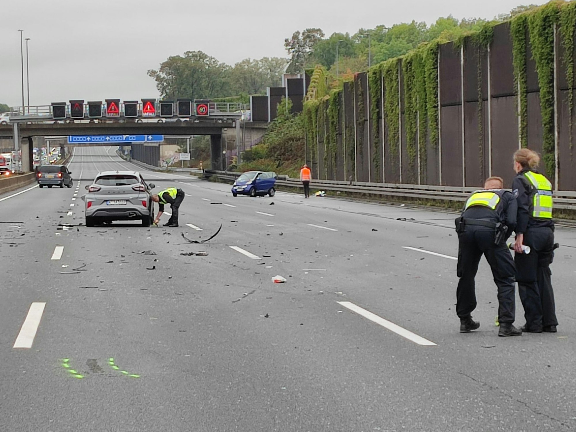 Die drei Unfallautos stehen umgeben von Trümmerteilen verteilt auf der Autobahn, Einsatzkräfte der Polizei stehen um die Autos herum.