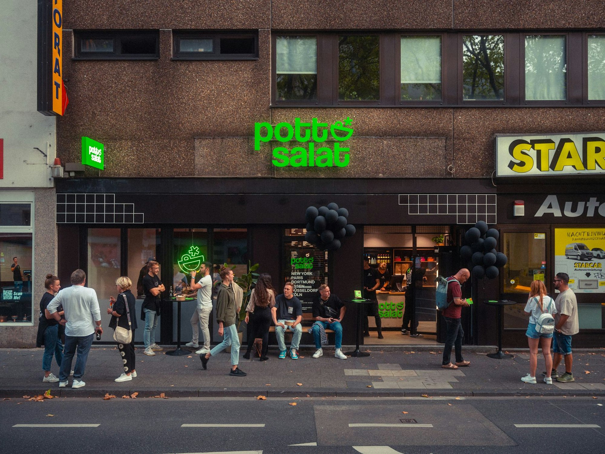 Menschen stehen und sitzen auf dem Bürgersteig vor der Pottsalat-Filiale.