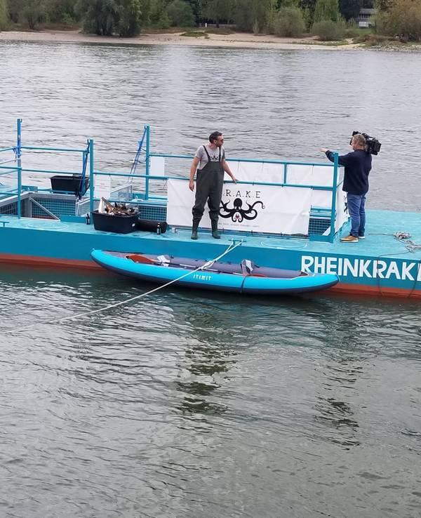 Ein blauer Ponton schwimmt auf dem Rhein bei Köln. Damit wird Müll aus dem Wasser gefischt.