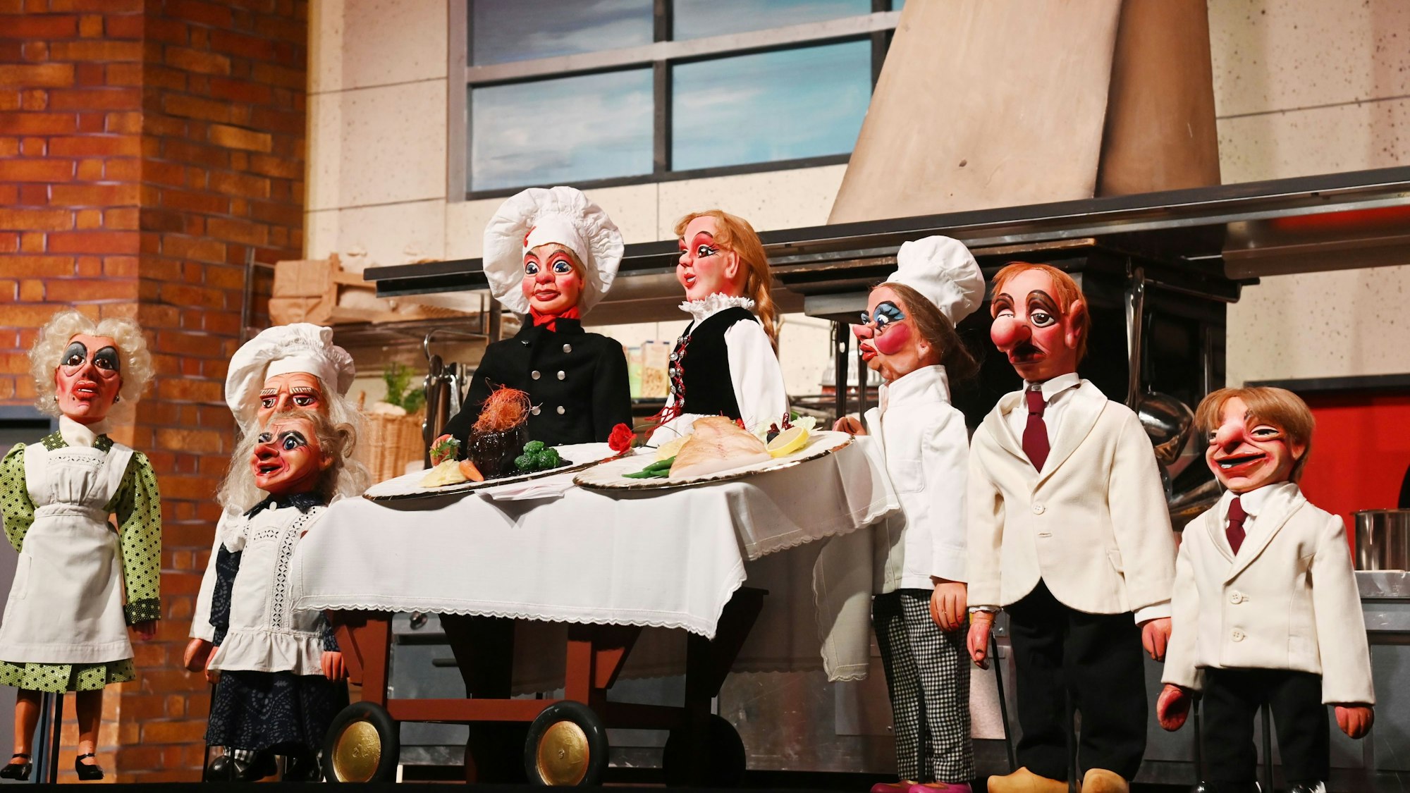 Puppen stehen als Köche verkleidet um einen gedeckten Tisch.