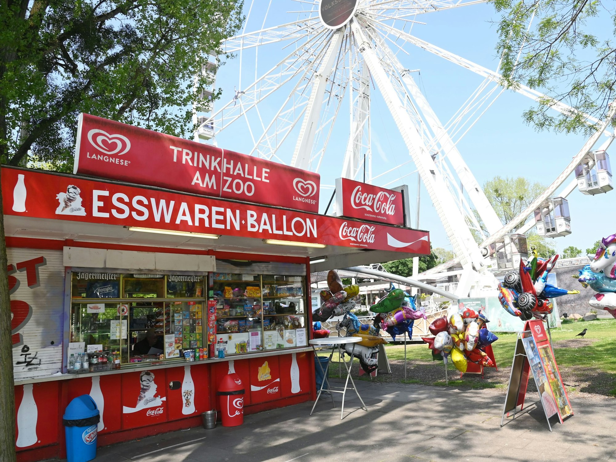 Büdchen mit Luftballons und Deko vor dem Riesenrad und dem Haupteingang des Kölner Zoos.