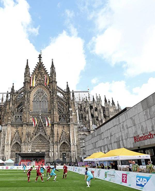 Fußballspieler spielen auf dem Fußballfeld vor dem Kölner Dom.