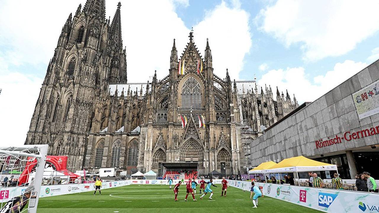 Fußballspieler spielen auf dem Fußballfeld vor dem Kölner Dom.
