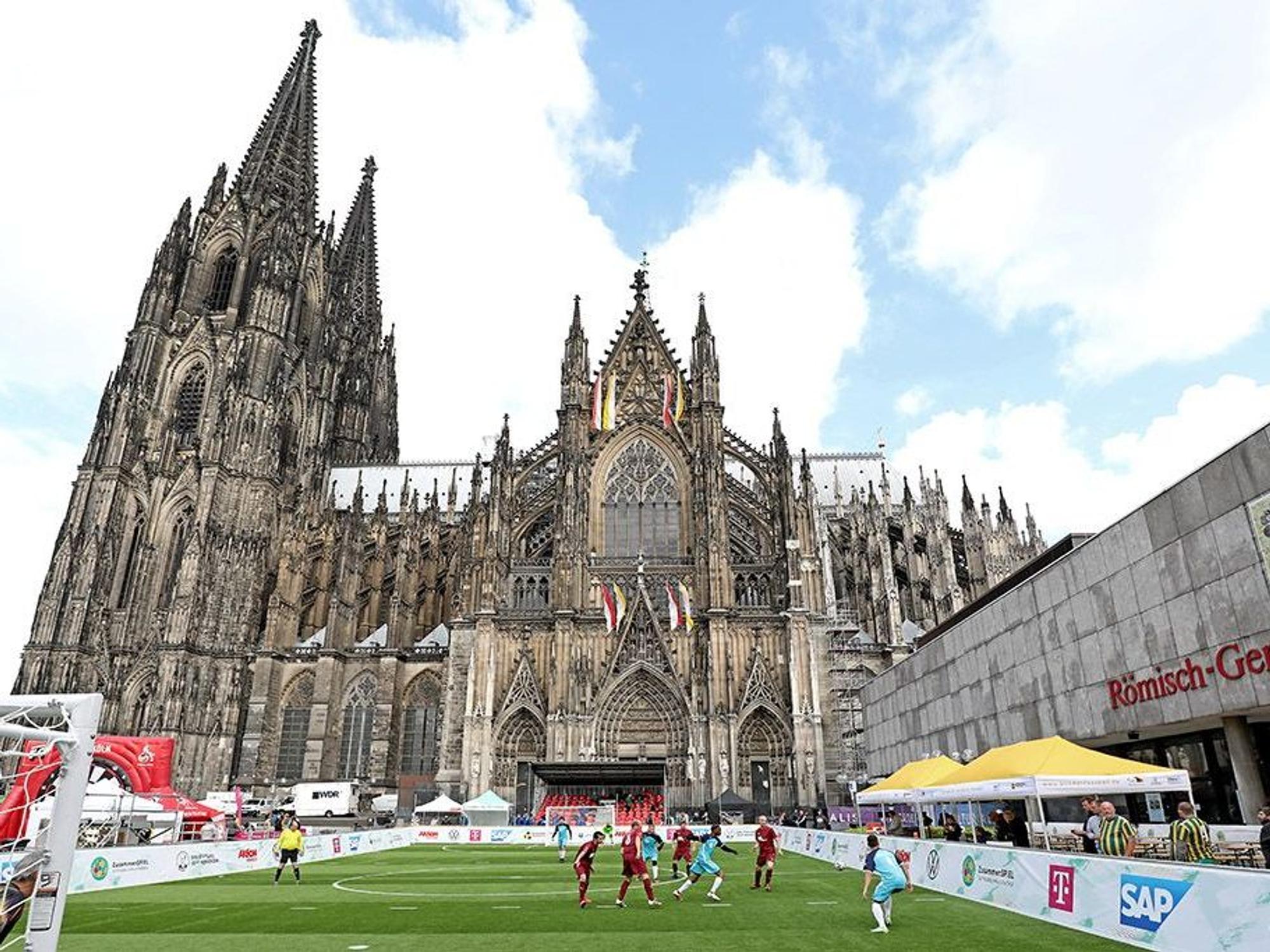 Fußballspieler spielen auf dem Fußballfeld vor dem Kölner Dom.
