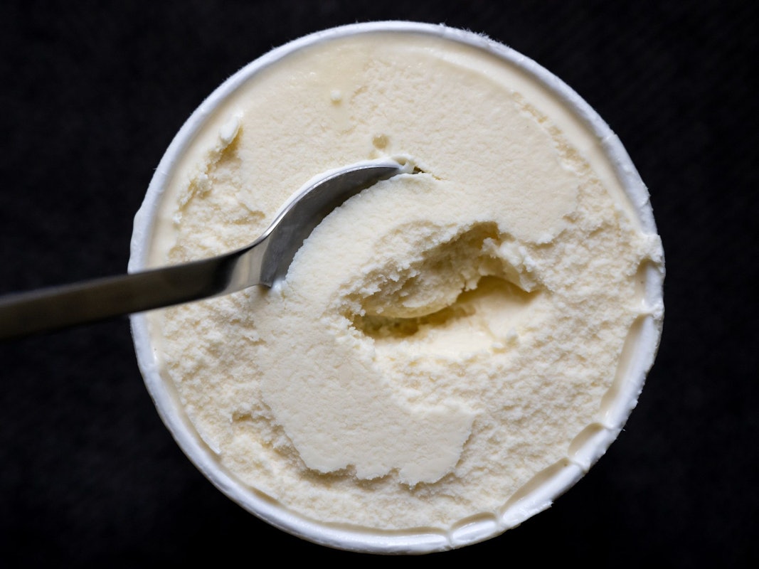 Ein Löffel steckt in einem Becher mit Vanilleeis.