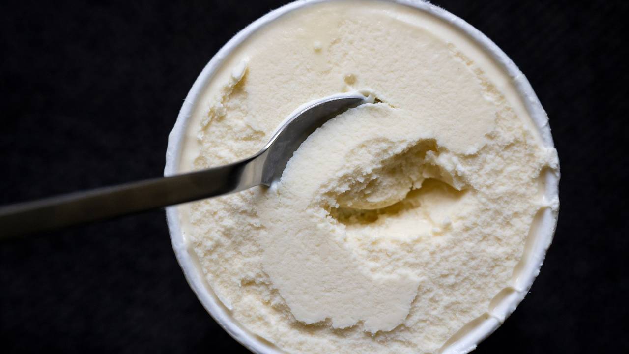 Ein Löffel steckt in einem Becher mit Vanilleeis.