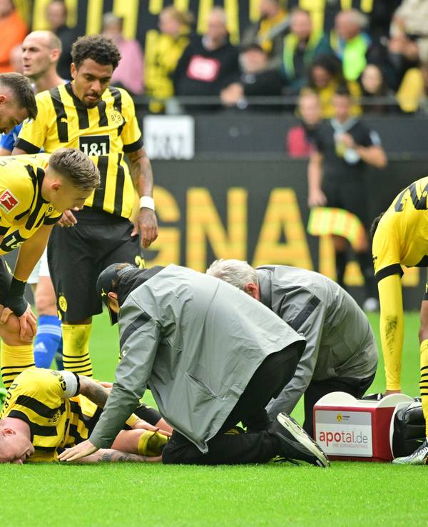 Marco Reus liegt auf dem Rasen und wird vom medizinischen Personal versorgt.