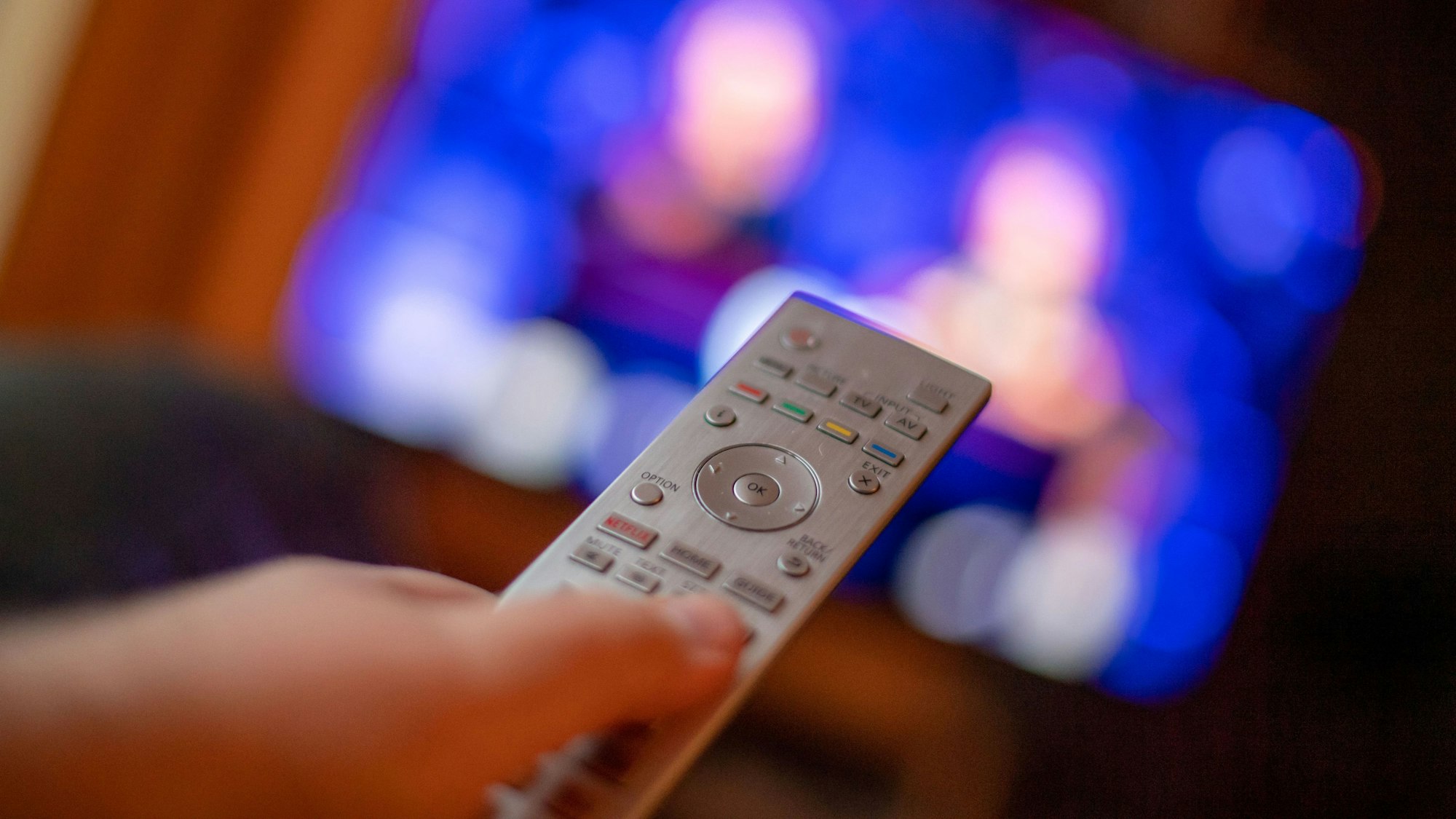 Ein Mann bedient mit der Fernbedienung einen Fernseher (gestellte Szene).