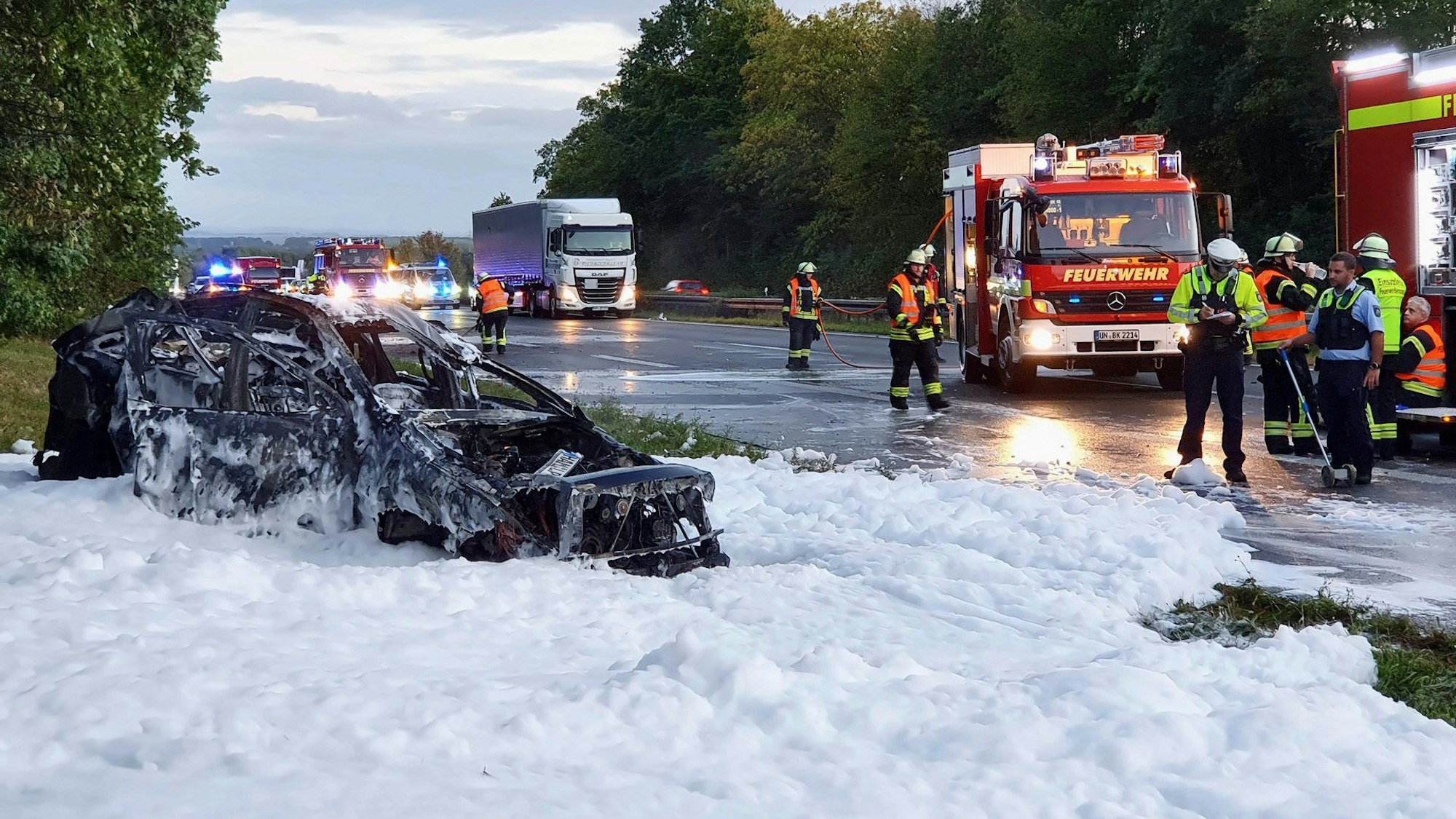 Das nach dem Unfall völlig ausgebrannte Autowrack steht noch in einem See aus Löschschaum neben der Autobahn A1.