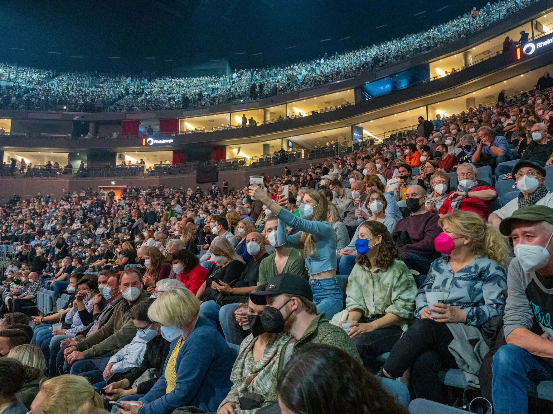 Fans auf der Tribüne der Lanxess-Arena in Köln verfolgen ein Konzert.