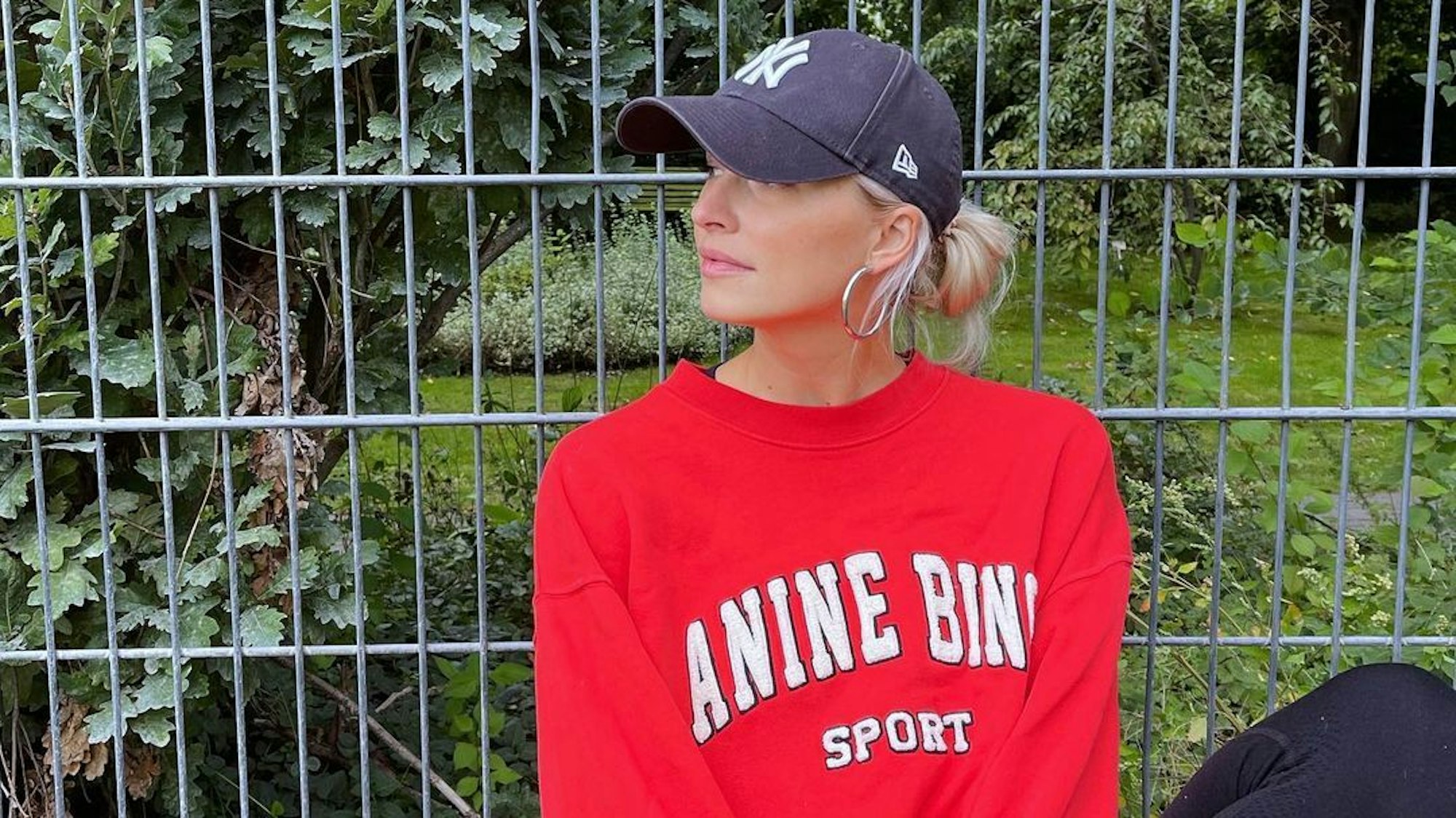 Moderatorin Lena Gercke, hier auf einem Instagram-Foto von September 2022, begeistert mit Babybauch-Beitrag ihre Fans auf Instagram. Auf dem Foto sitzt Lena vor einem Zaun. Sie trägt einen roten Pullover und ein schwarzes Käppi.