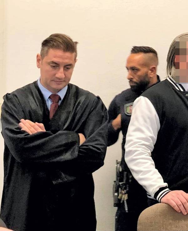 Der Angeklagte steht zwischen seinen beiden Verteidigern.