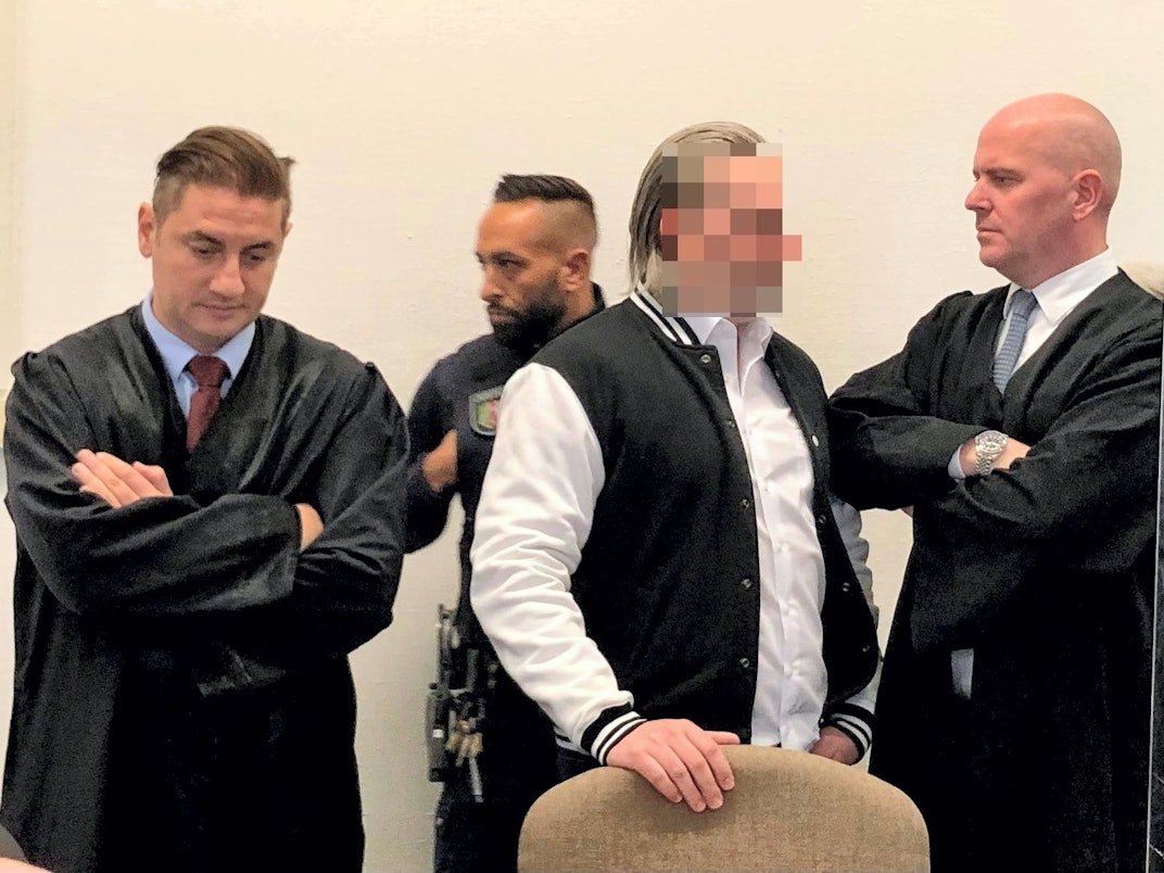 Der Angeklagte steht zwischen seinen beiden Verteidigern.