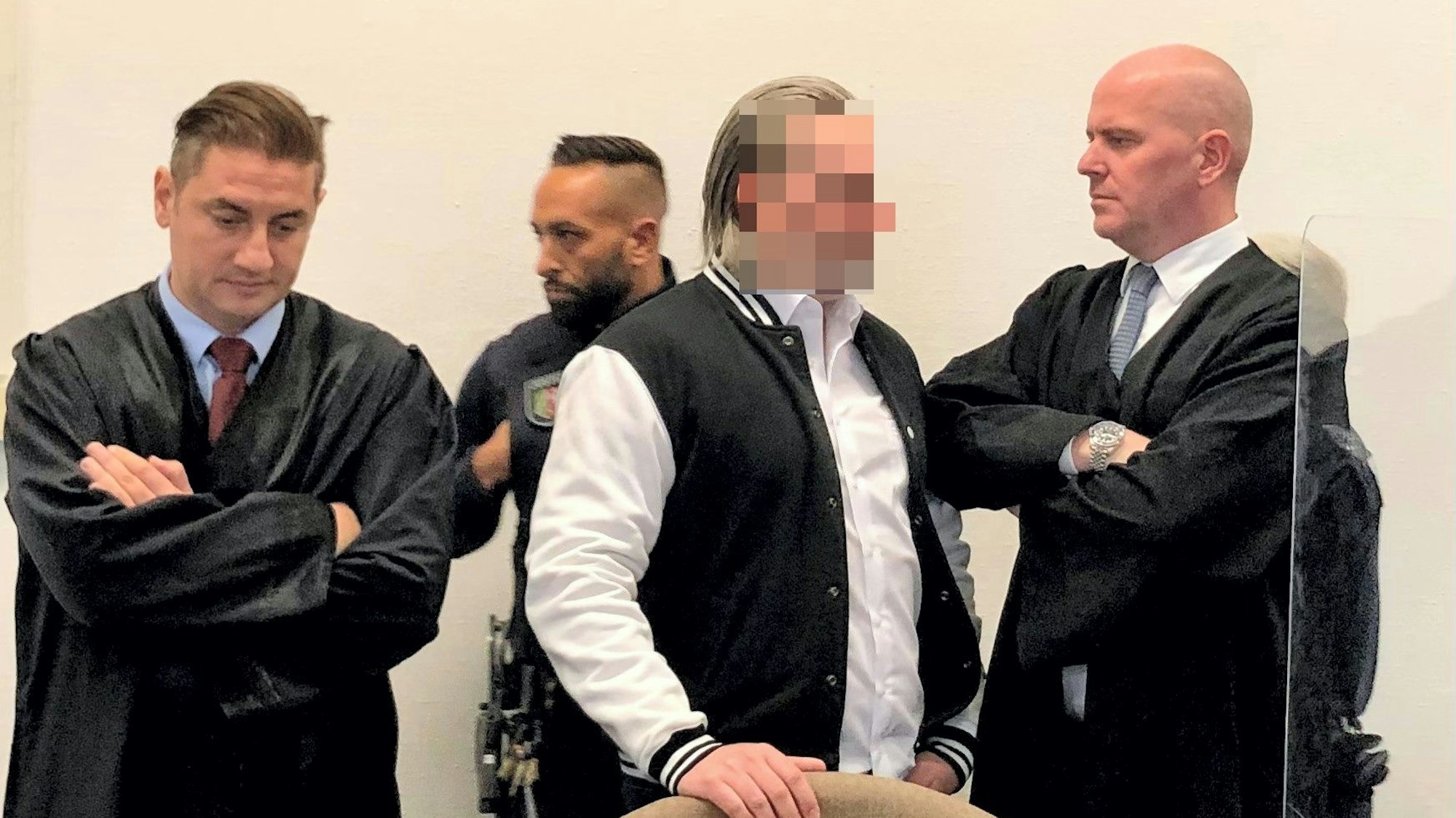 Der Angeklagte steht zwischen seinen beiden Verteidigern.