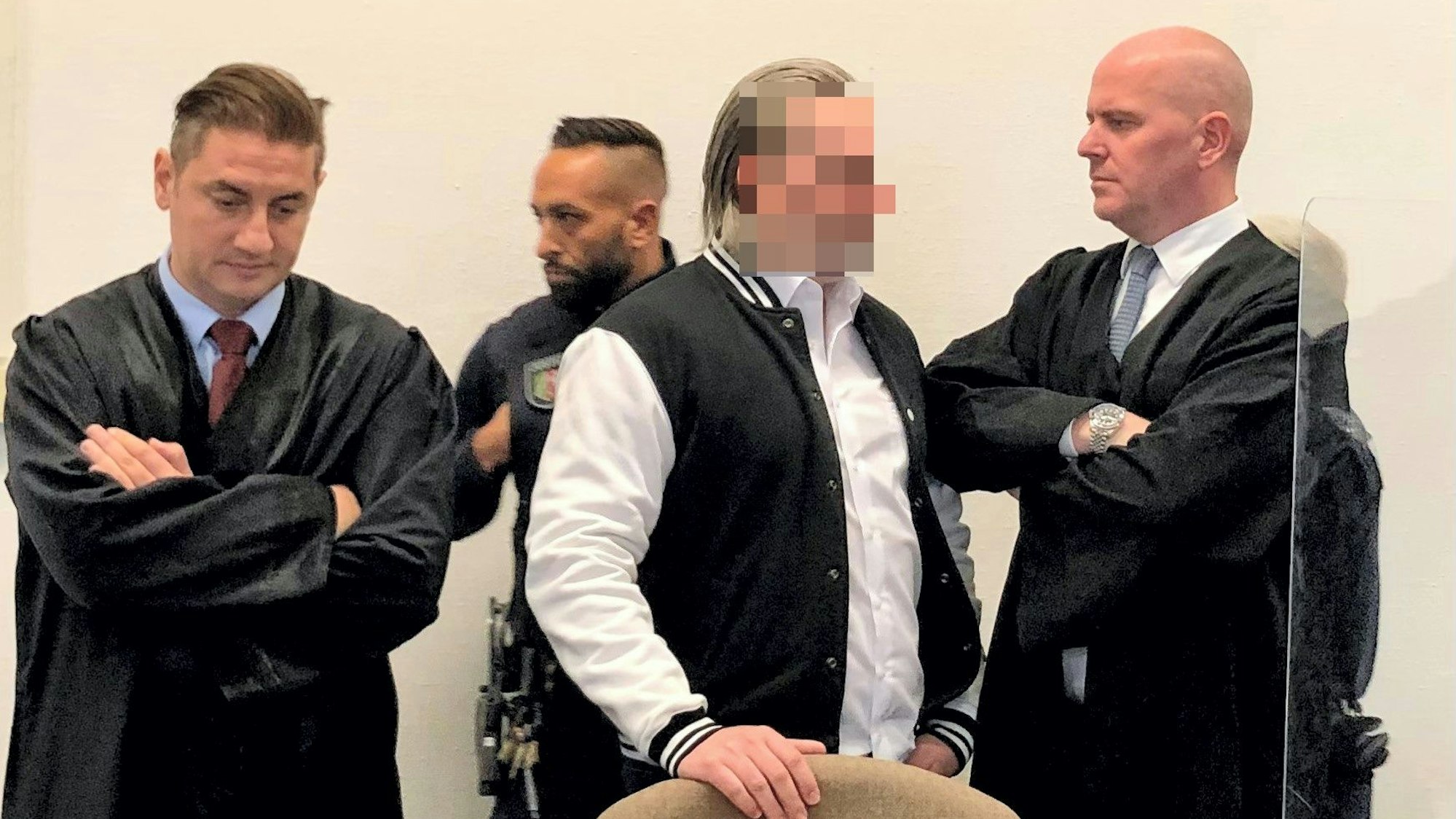 Der Angeklagte steht zwischen seinen beiden Verteidigern.