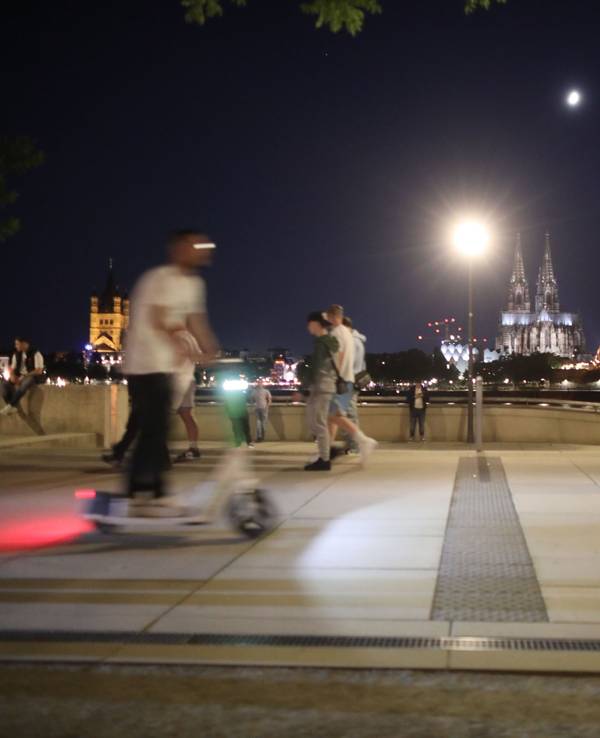 Am Rheinboulevard ist ein Mann mit einem E-Scooter zwischen Fußgängern unterwegs.