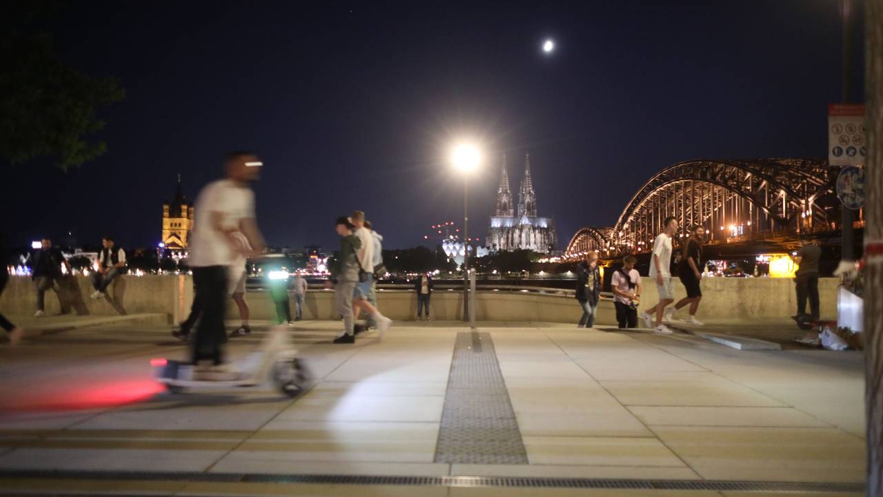 Am Rheinboulevard ist ein Mann mit einem E-Scooter zwischen Fußgängern unterwegs.