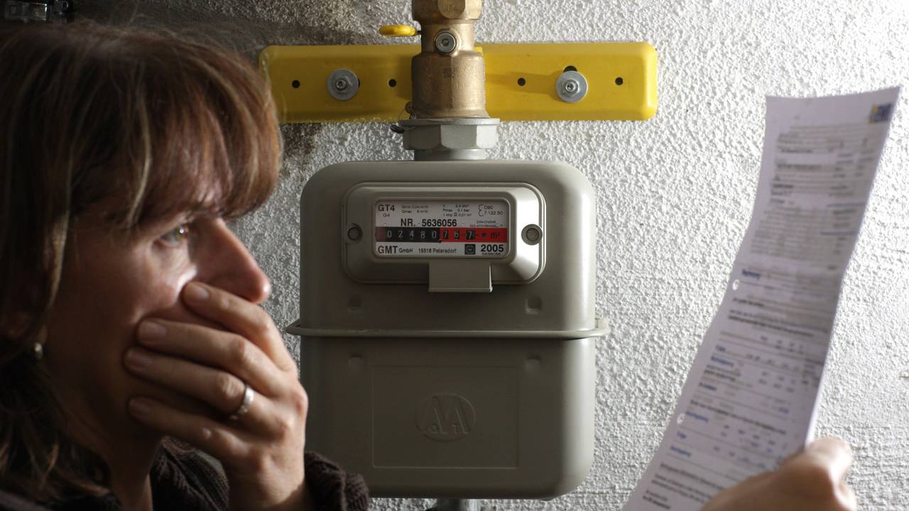 Immer mehr Gasanbieter versuchen Kundinnen und Kunden in eine deutlich teurere Ersatzversorgung zu schieben. Eine Frau steht in unserem Symbolbild neben einem Gaszähler und blickt erschrocken auf die hohe Abrechnung des Energieversorgers.