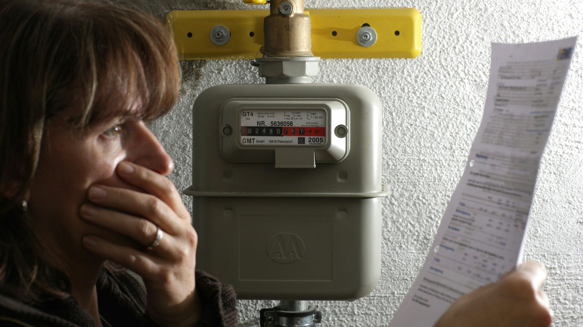 Immer mehr Gasanbieter versuchen Kundinnen und Kunden in eine deutlich teurere Ersatzversorgung zu schieben. Eine Frau steht in unserem Symbolbild neben einem Gaszähler und blickt erschrocken auf die hohe Abrechnung des Energieversorgers.