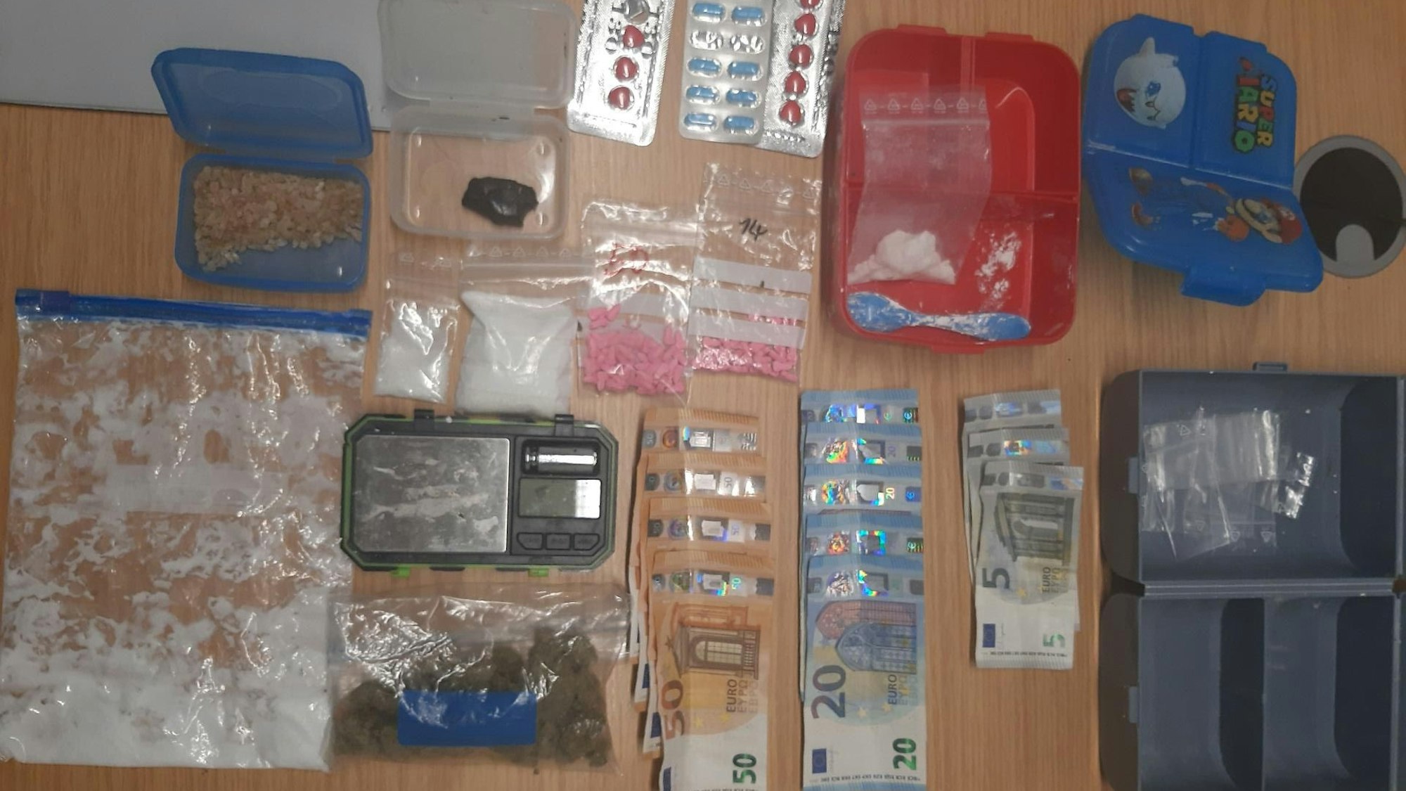 Auf einem Tisch liegen Beutel mit Drogen, Pillen sowie Bargeldscheine.