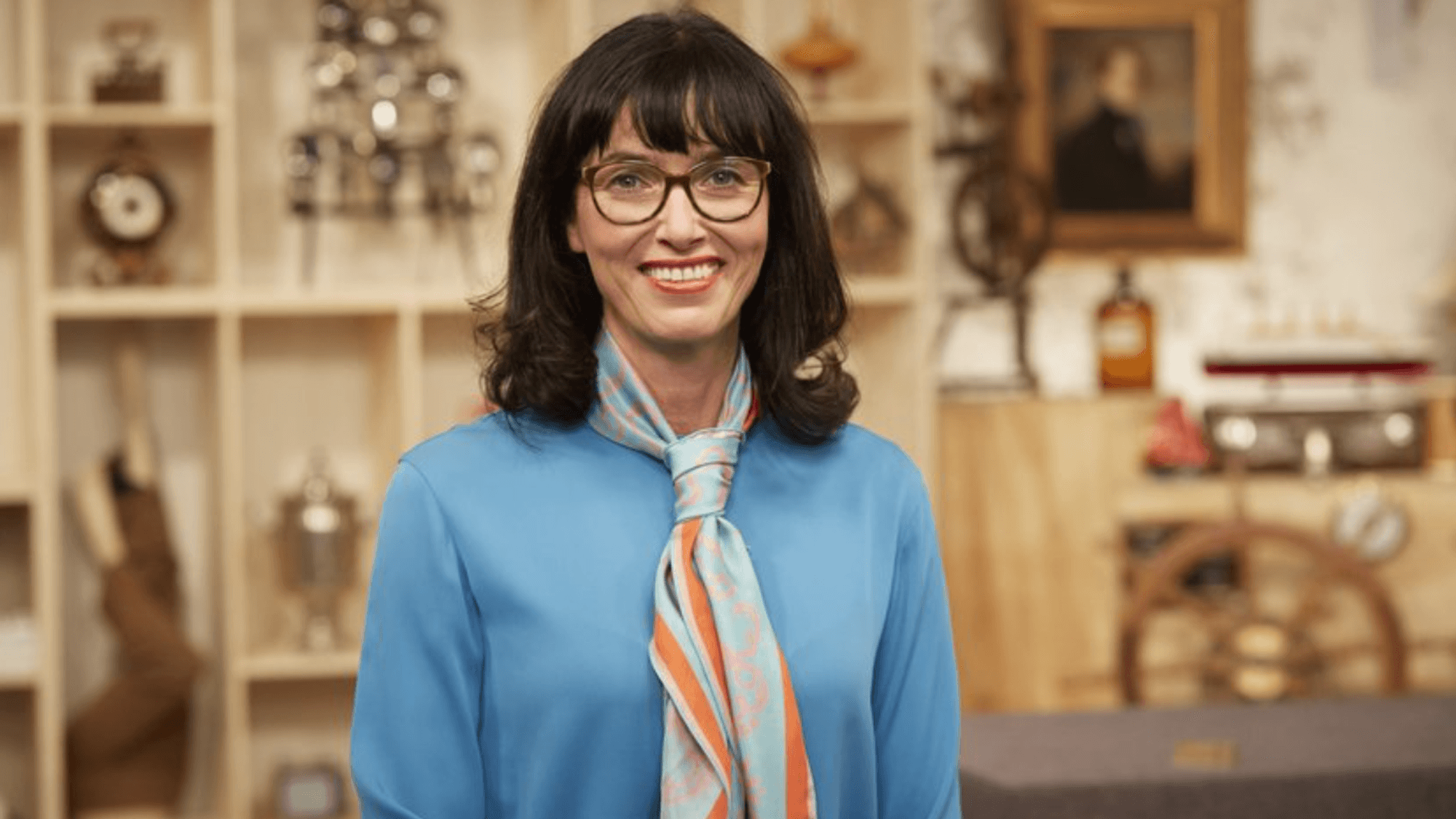 Auf dem Bild sehen Sie Expertin Dr. Heide Rezepa-Zabel, die die Rarität von Susanne bewertet. Heide Rezepa-Zabel trägt einen hellblauen Pullover und ein hellblau-orangenes Tuch.