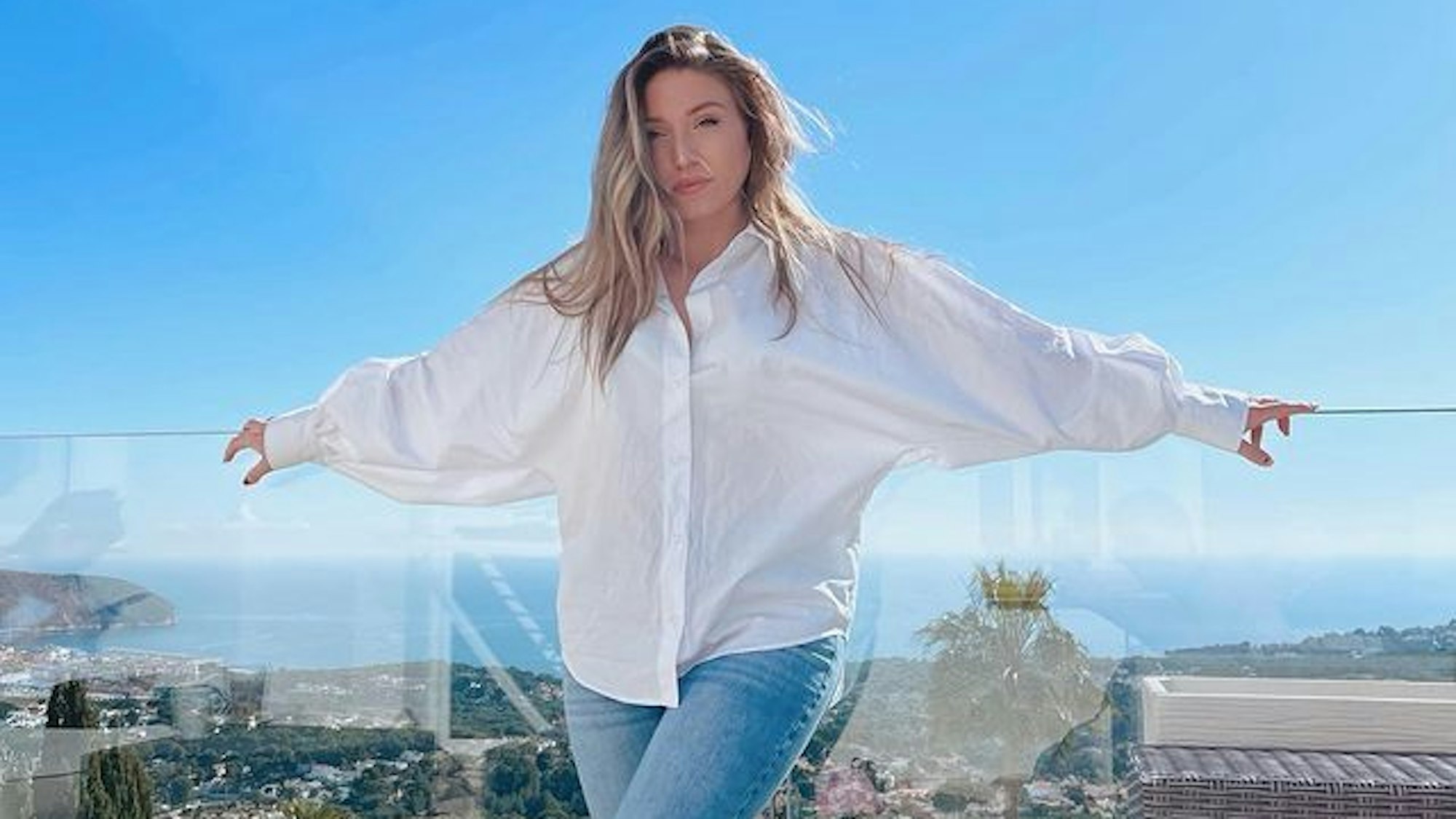 Biancas Noch-Ehemann Julian Claßen verrät im Interview, wie es der YouTuberin, hier auf einem Instagram Foto von Februar 2022, wirklich geht. Auf dem Foto steht Bianca in Jeans und weißer Bluse vor einer Glas-Ballustrade. Im Hintergrund ist das Meer zu sehen.