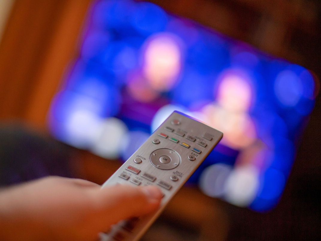 Ein Mann bedient mit der Fernbedienung einen Fernseher (gestellte Szene).