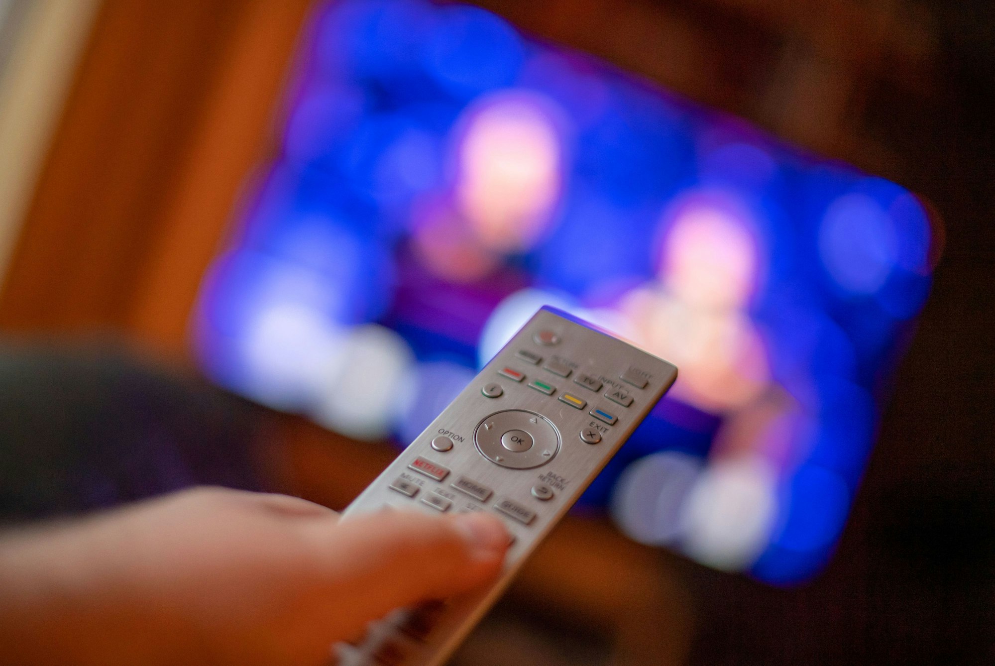 Ein Mann bedient mit der Fernbedienung einen Fernseher (gestellte Szene).