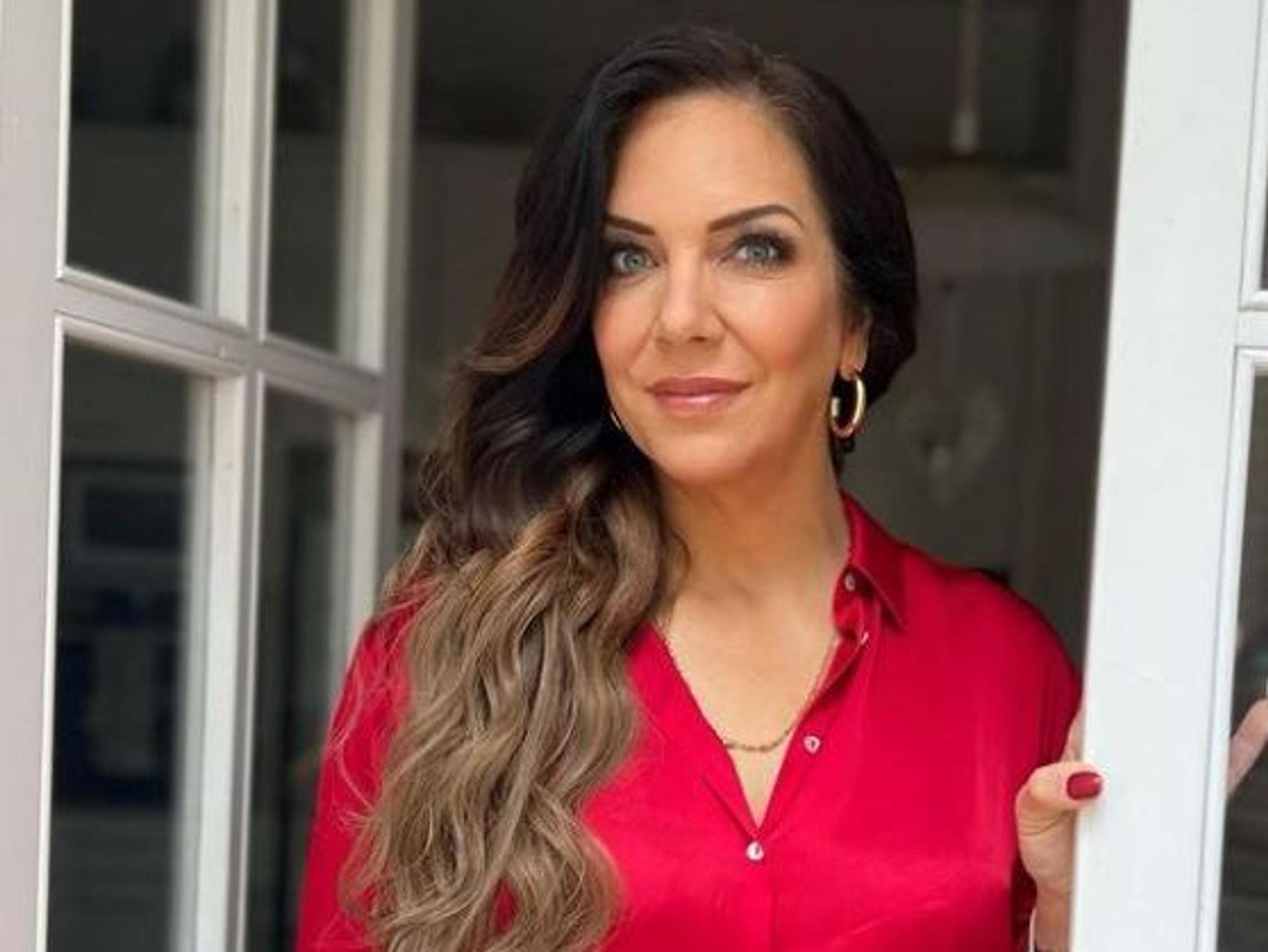 Danni Büchner posiert an einem Fenster in einem roten Oberteil.