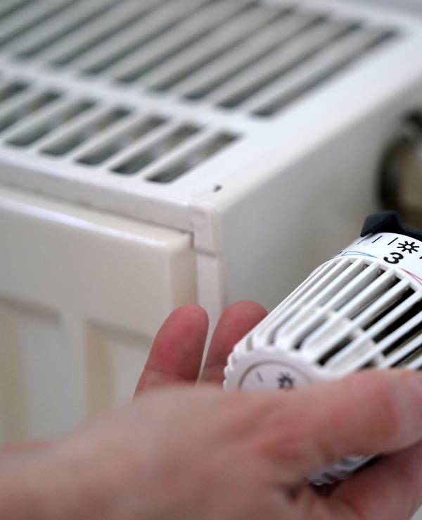 Eine Frau dreht an einem Heizungsthermostat.