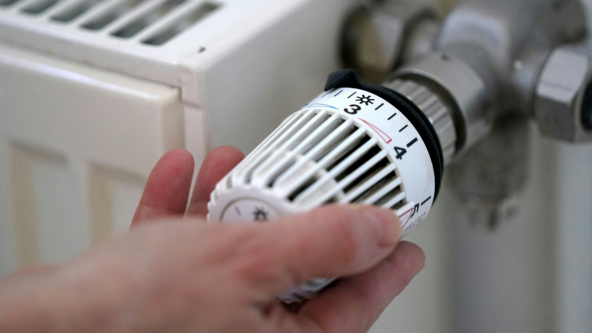 Eine Frau dreht an einem Heizungsthermostat.