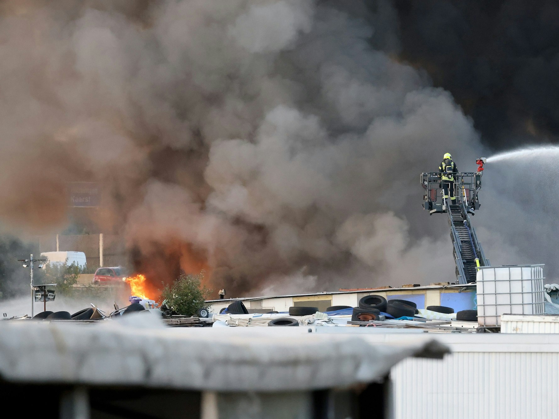 Feuerwehrkräfte bekämpfen von einer Drehleiter einen Brand auf einem Schrottplatz. Ein Brand auf einem Schrottplatz zwischen Neuss und Kaarst hat am Donnerstagabend eine mächtige und weithin sichtbare Rauchsäule erzeugt.
