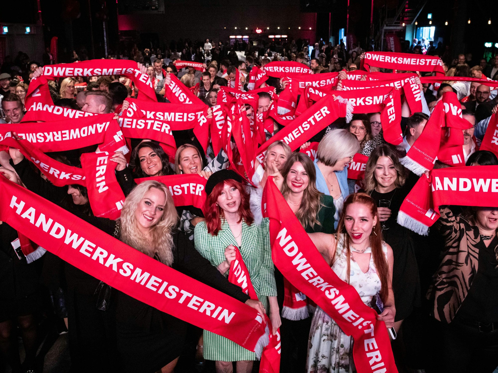 Junge Frauen und Männer halten bedruckte Schals in die Kamera und freuen sich über ihre Auszeichnung.