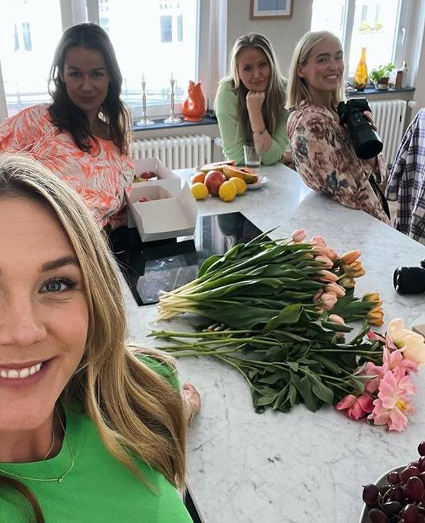 Alina Merkau macht ein Selfie. Im Hintergrund stehen drei weitere Frauen. Hinter ihr auf der Küchenarbeitsplatte liegen verschiedene Blumen.