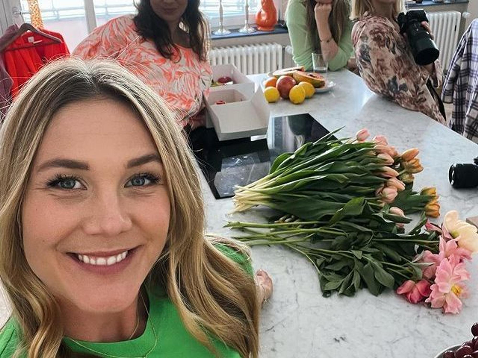 Alina Merkau macht ein Selfie. Im Hintergrund stehen drei weitere Frauen. Hinter ihr auf der Küchenarbeitsplatte liegen verschiedene Blumen.
