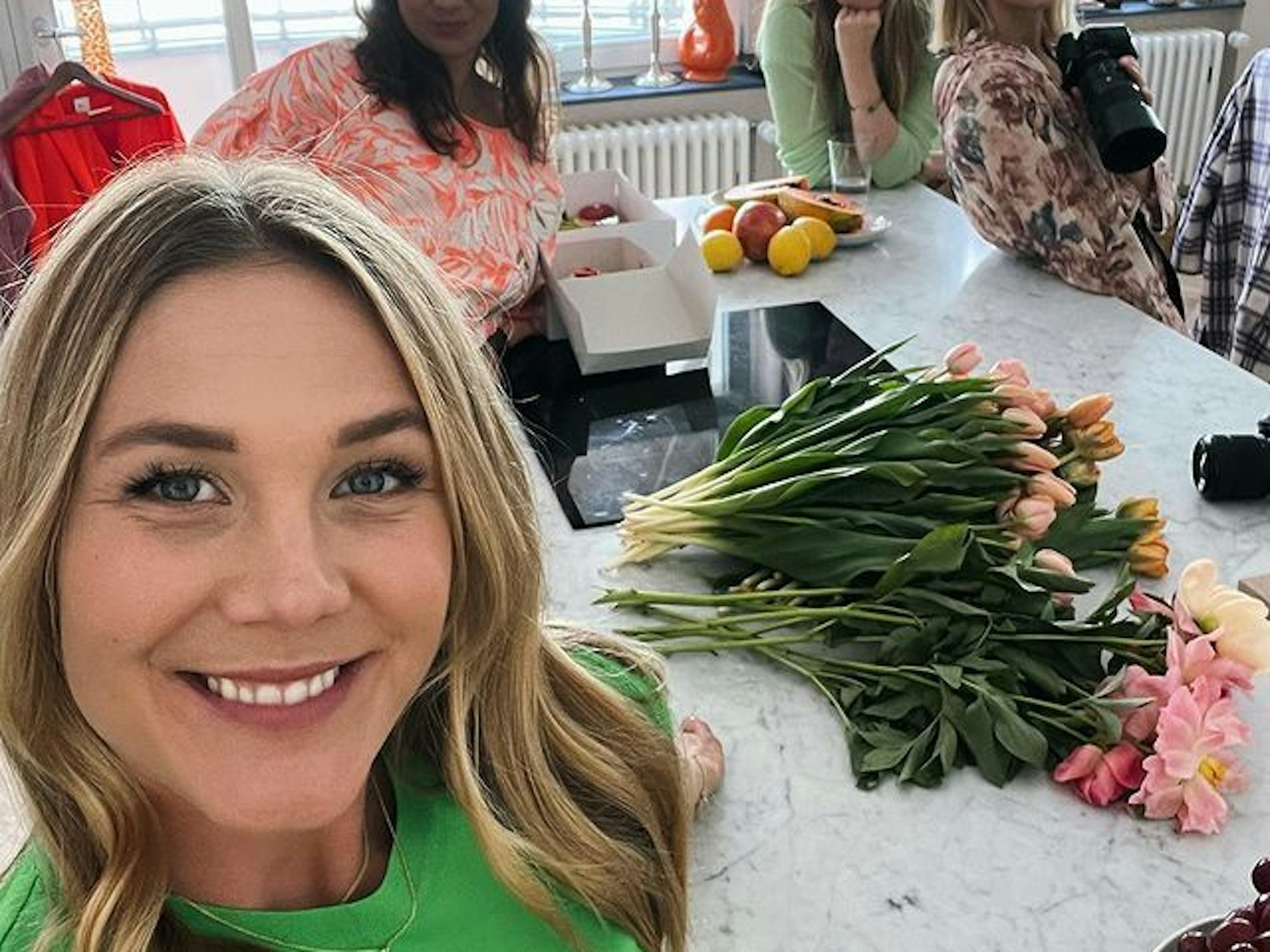 Alina Merkau macht ein Selfie. Im Hintergrund stehen drei weitere Frauen. Hinter ihr auf der Küchenarbeitsplatte liegen verschiedene Blumen.