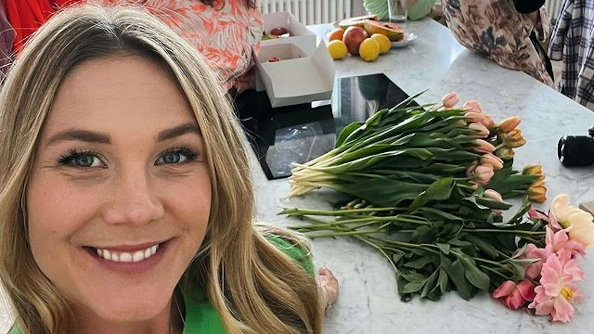 Alina Merkau macht ein Selfie. Im Hintergrund stehen drei weitere Frauen. Hinter ihr auf der Küchenarbeitsplatte liegen verschiedene Blumen.