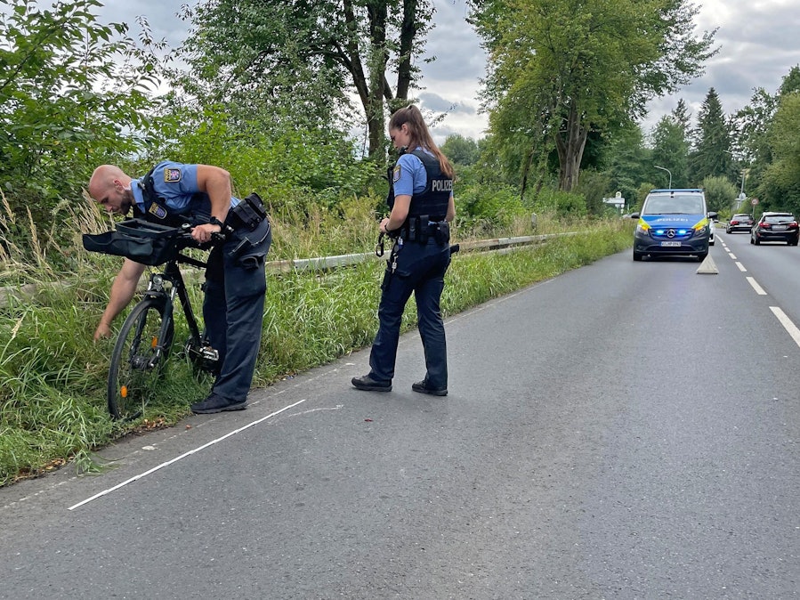 Die Polizistin Milena und der Polizist Dominique inspizieren ein Fahrrad, das in einen Unfall verwickelt ist. Im Hintergrund steht ein Polizeiauto.