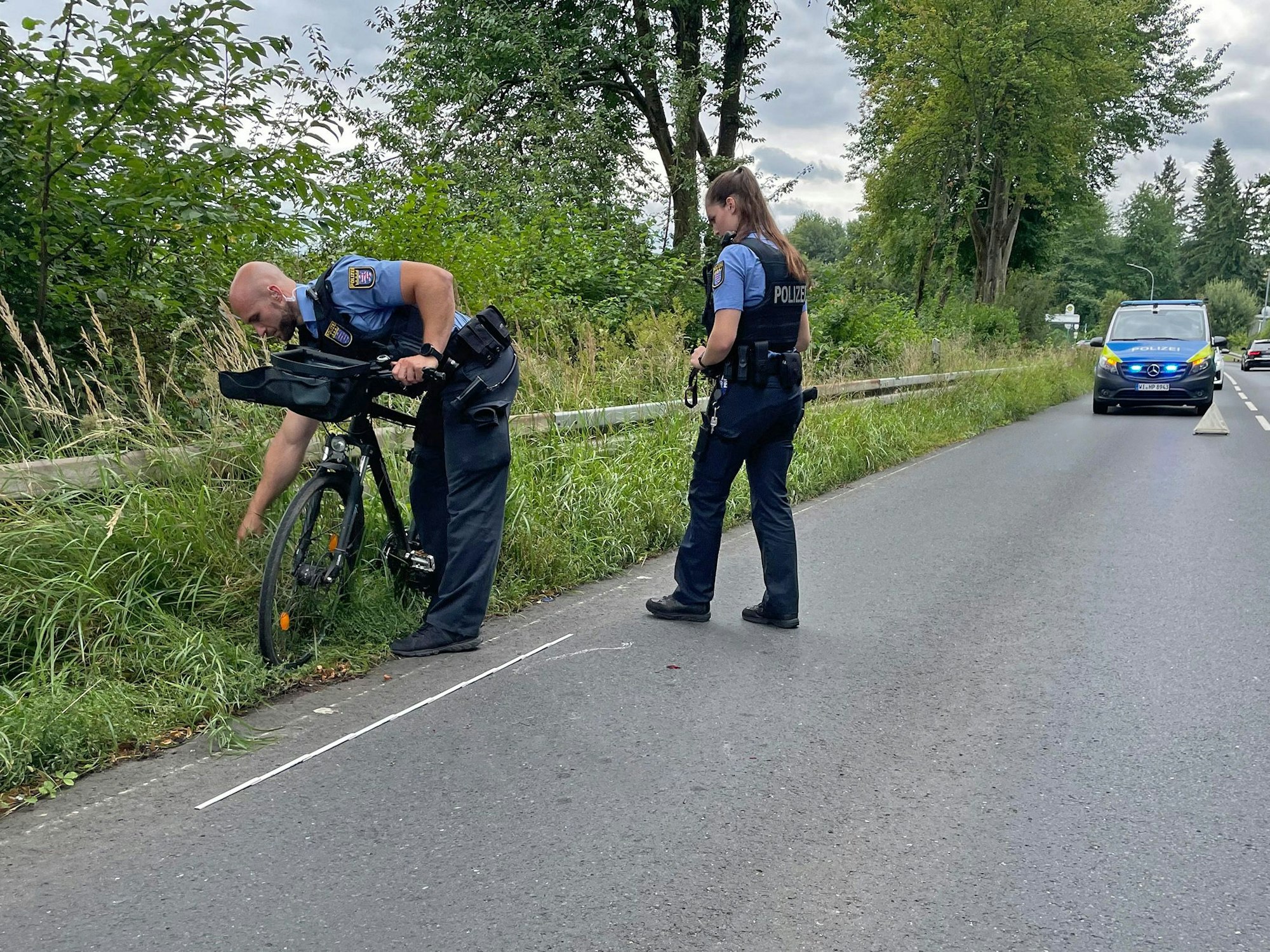 Die Polizistin Milena und der Polizist Dominique inspizieren ein Fahrrad, das in einen Unfall verwickelt ist. Im Hintergrund steht ein Polizeiauto.
