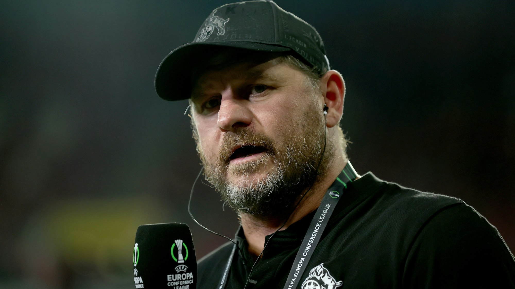 Steffen Baumgart vor einem Spiel mit Mikrofon in der Hand.