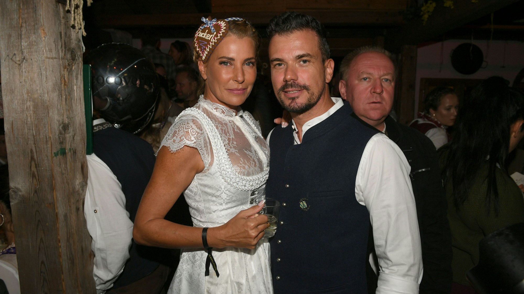 Auf dem Bild stehen Giulia und Ludwig Arm in Arm und posieren für die Kamera. Giulia trägt ein weißes Dirndl mit weißer Spitzenbluse, ihr Freund Ludwig ein weißes Hemd und eine Trachtenjacke.