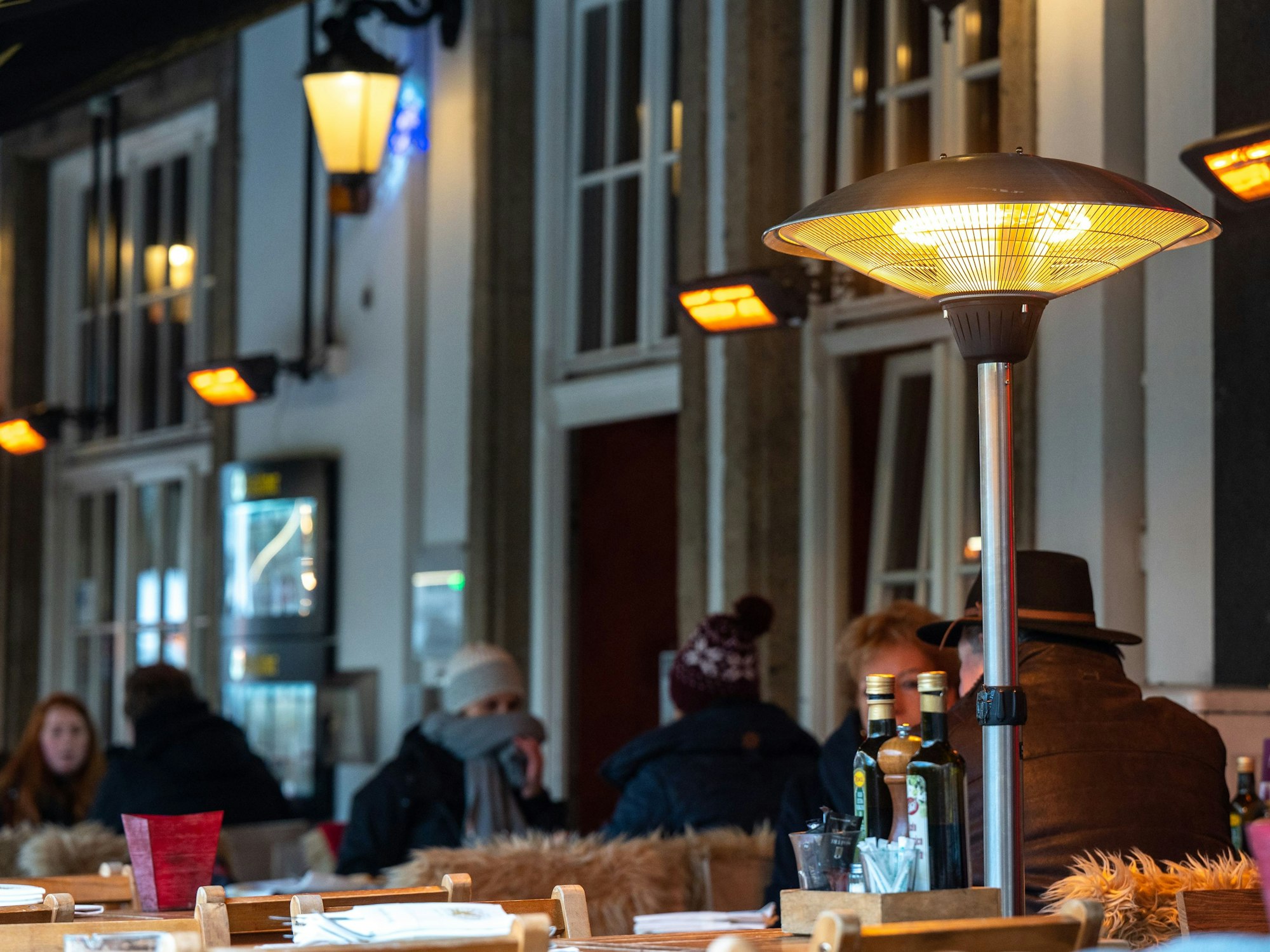 Restaurantbesucher sitzen im Winter unter Wärmelampen in der Außengastronomie.