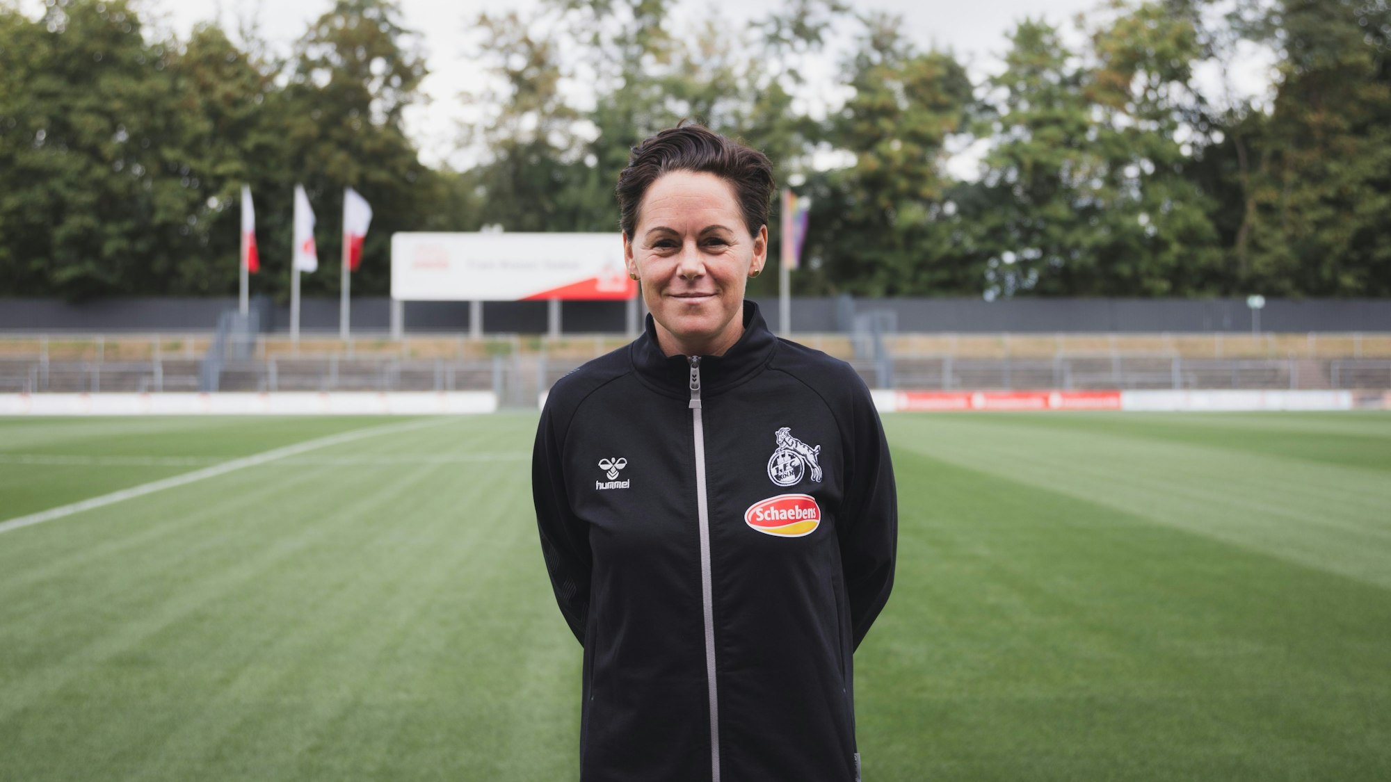 Leiterin der Frauen des 1. FC Köln, Nicole Bender, lächelt auf dem Fußballplatz in die Kamera.