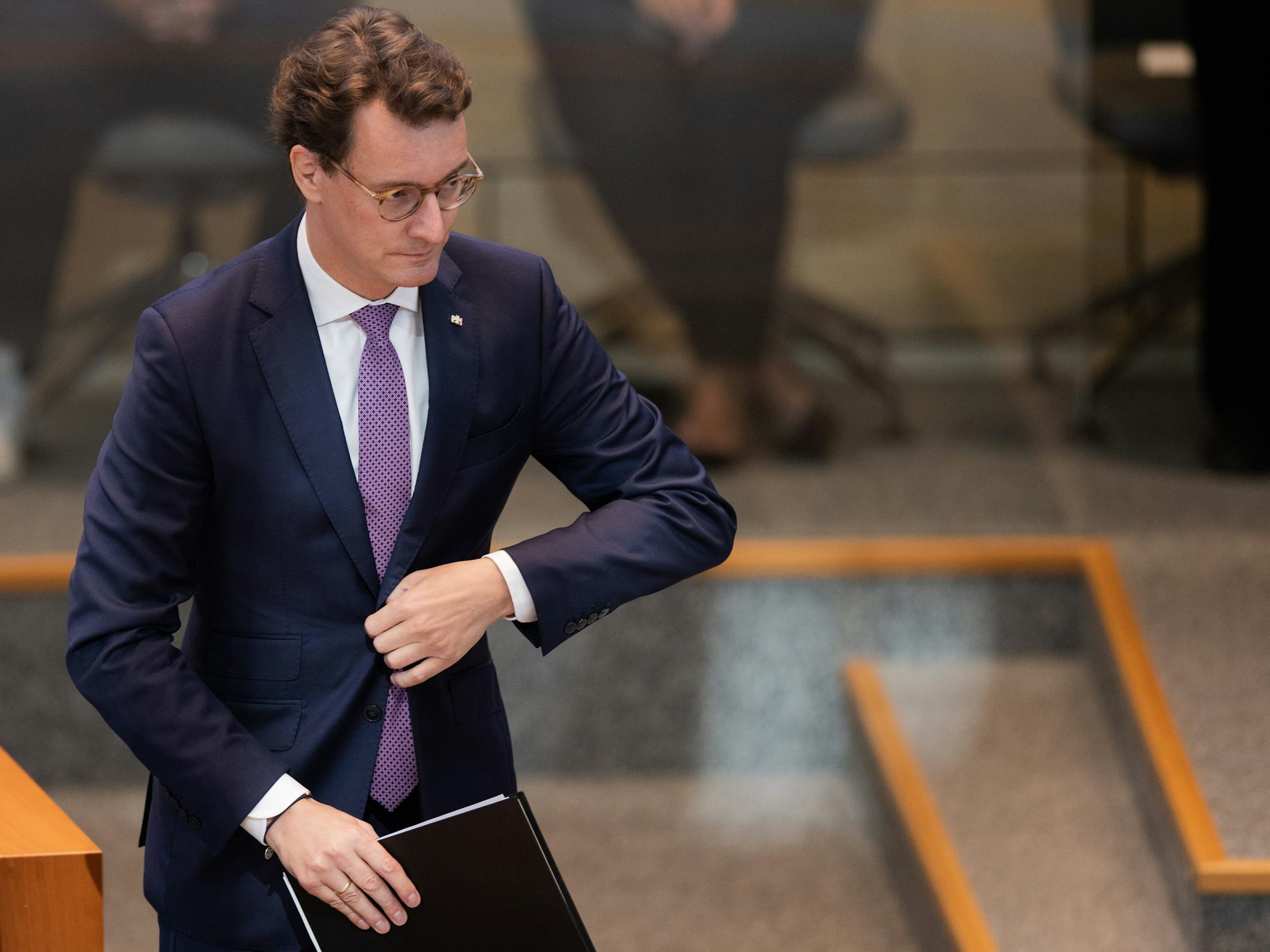Hendrik Wüst, Ministerpräsident von Nordrhein-Westfalen, geht zum Rednerpult im Plenum des Landtags und knöpft sich dabei das Jackett zu.