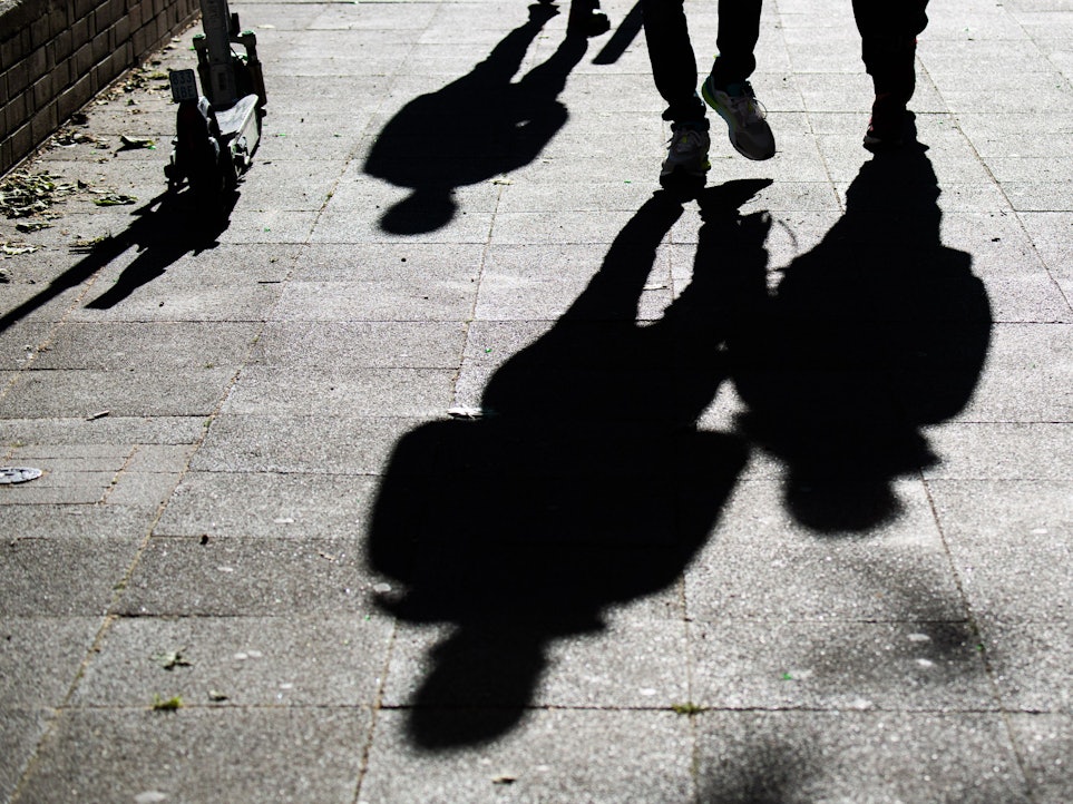 Schüler gehen am Morgen zur Schule und werfen dabei ihre Schatten auf den Gehweg.