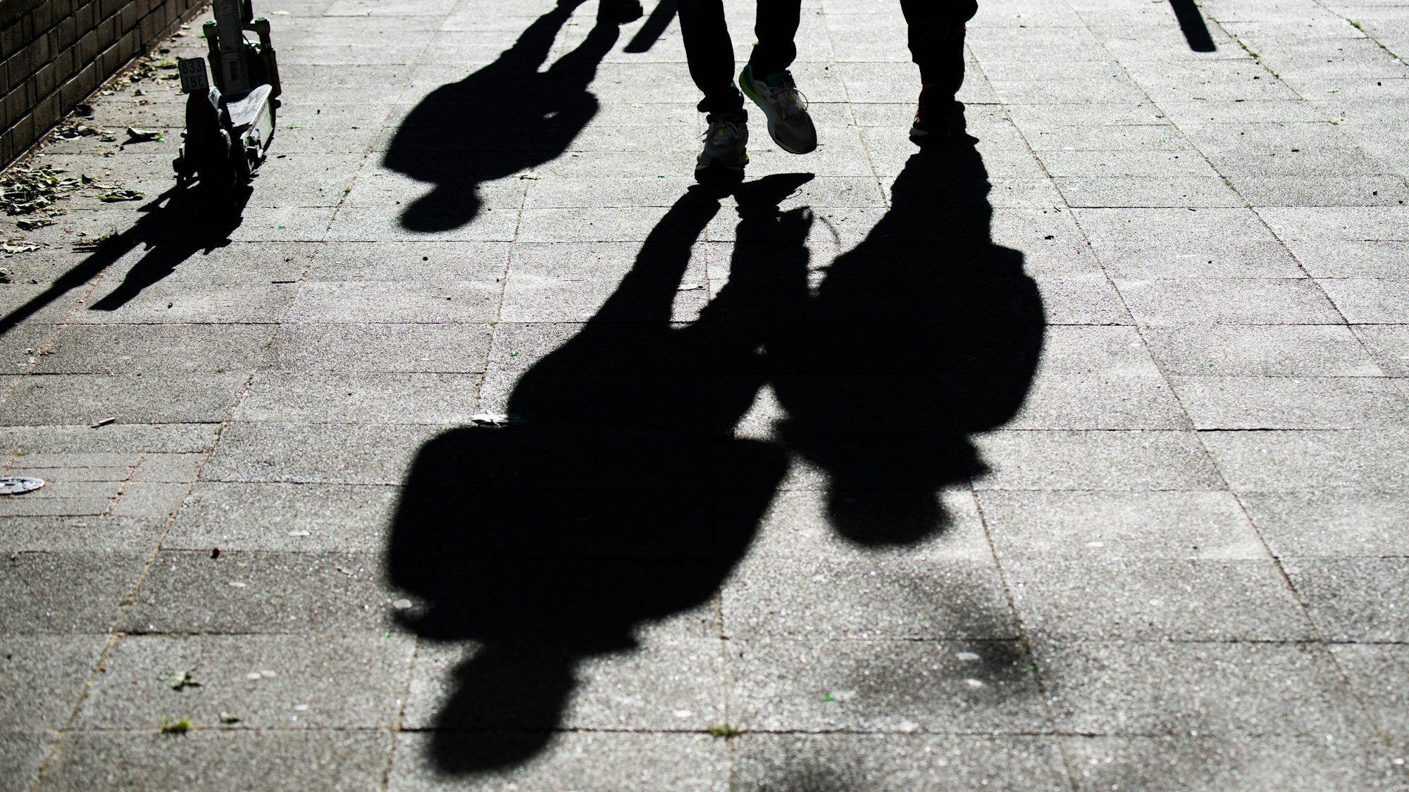 Schüler gehen am Morgen zur Schule und werfen dabei ihre Schatten auf den Gehweg.
