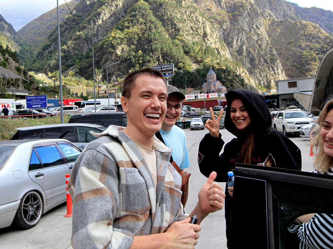 Eine Gruppe von Russinnen und Russen lächelt am Grenzübergang Werchni Lars zwischen Georgien und Russland am Freitag (23. September 2022). Auch dort haben sich lange Fahrzeugschlangen gebildet, nachdem Putin eine Teilmobilisierung in seinem Land angekündigt hatte.